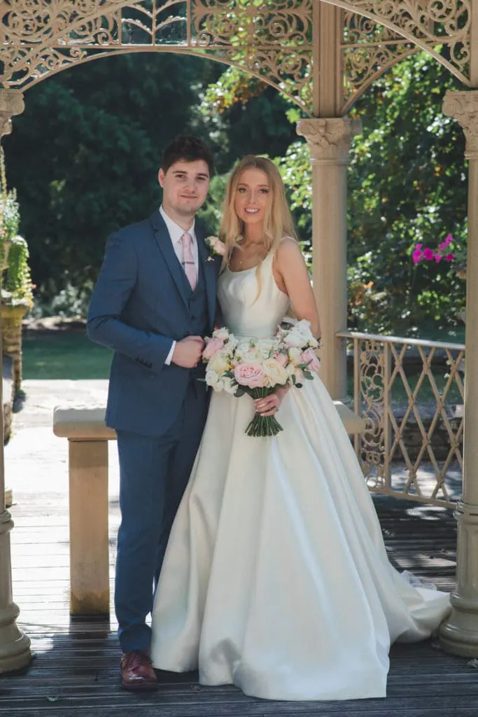 Classic wedding photography style of a bride and groom posing underneath an arbour in a pretty garden