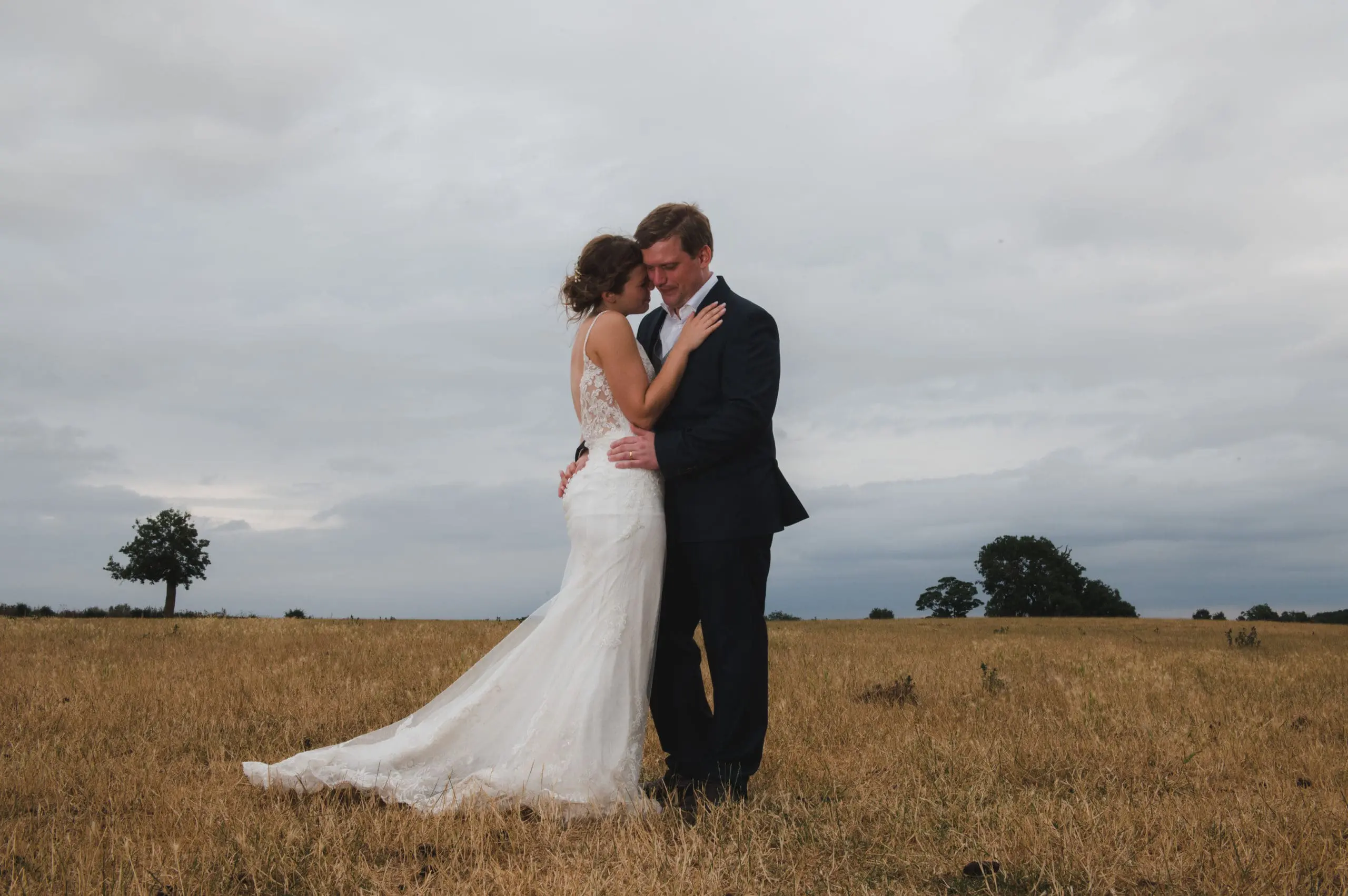 DSC_0534 A bridal couple are embracing in the middle of a parched, grassy meadow - Bedfordshire Wedding Photographer