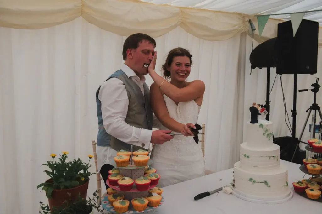 Hiring a professional wedding photographer - a bride squashes some of the wedding cake onto her grooms face