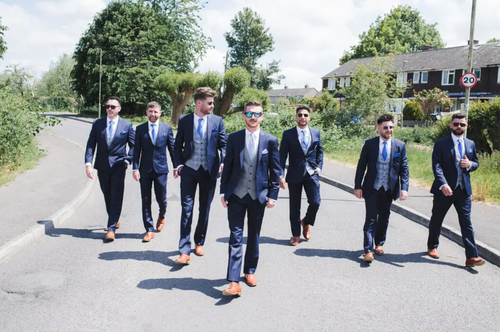 hiring a professional wedding photographer - a groom and his groomsmen, smartly dressed and wearing sunglasses are walking down the road