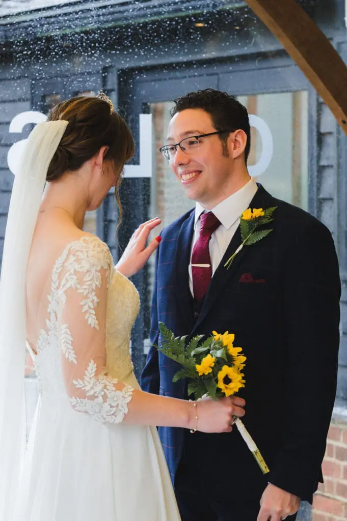 Bedford wedding photographer - A bride, holding sunflowers, places her hand on her Grooms' shoulder as he smiles lovingly a her