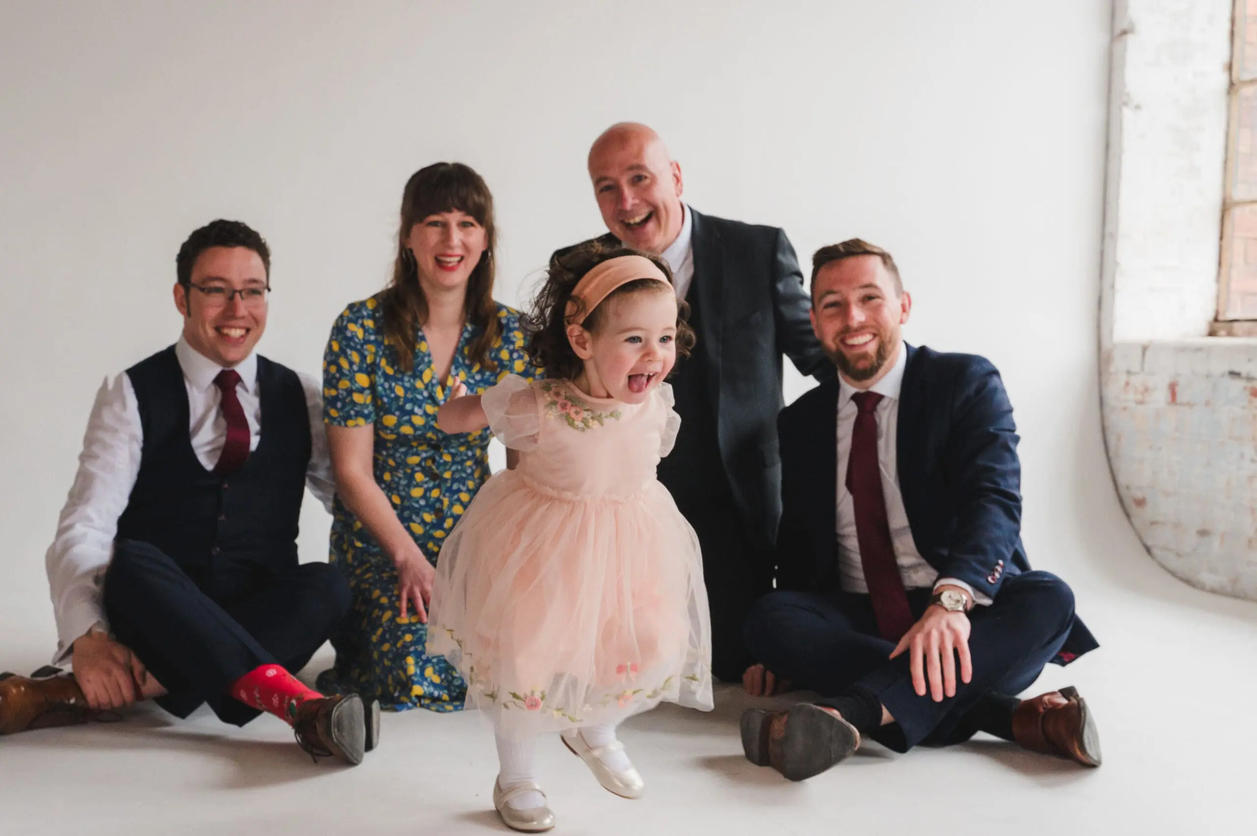 Bedfordshire Family Photography Professional Family Photography prices Bedfordshire a family sat on the floor with a little girl running forward in a pretty apricot dress