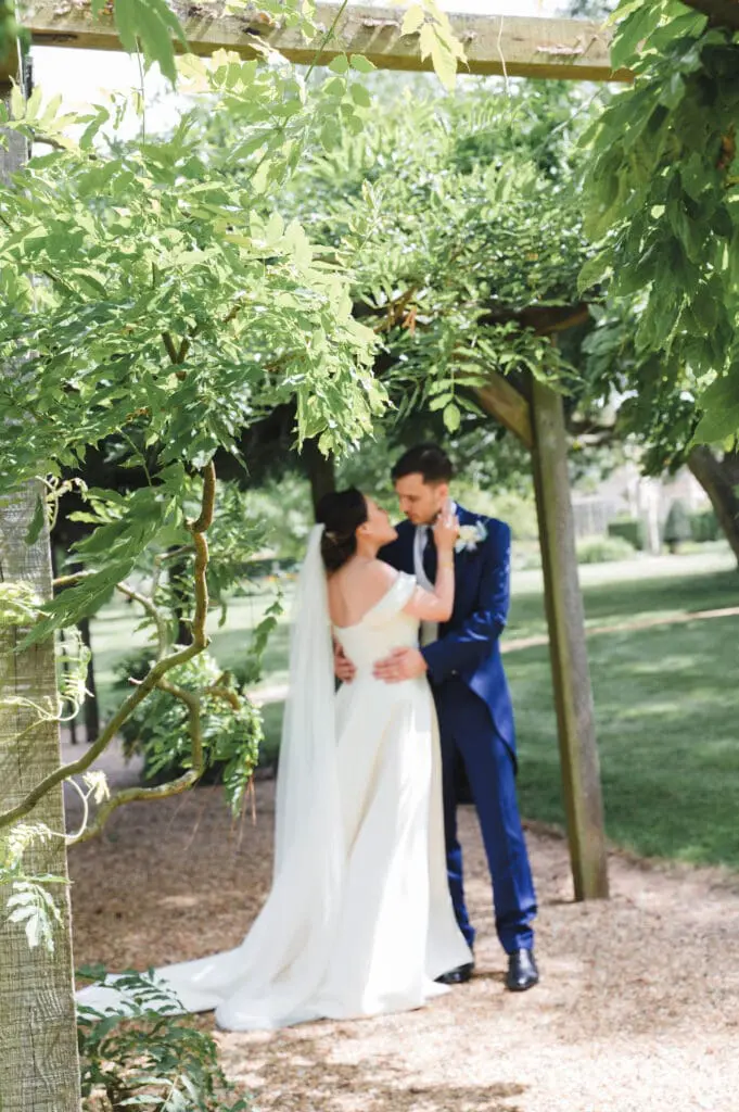 bride and groom holding each other under a trellis arch covered in plants at their perfect wedding venue