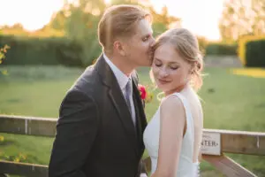 Catherine Brooks Photography captured a tender kiss by the groom on the top of the bride's head as the sun sets - they are next to a gate/field