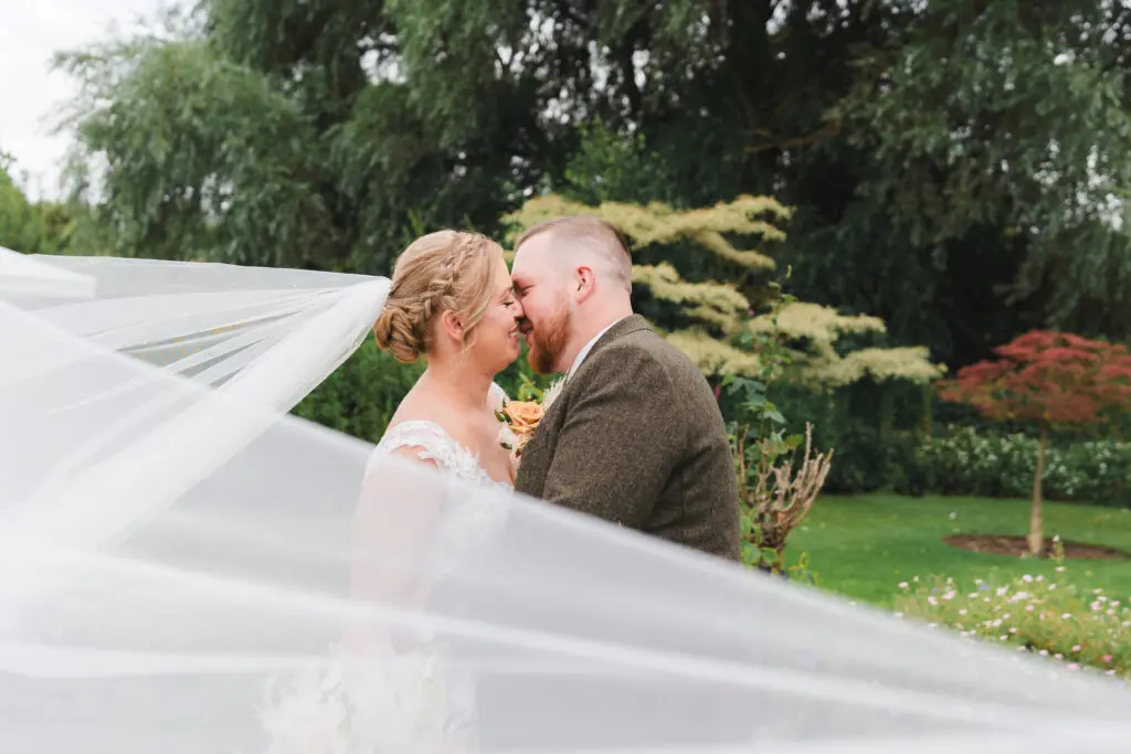 Wedding in Bedfordshire Bride and groom kissing in the grounds of their venue, the brides veil is sweeping in the wind
