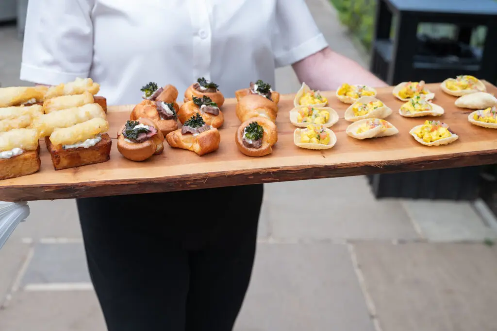 a caterer with canapes on a wooden platter - manage a wedding budget