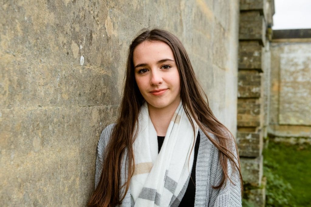 Families portfolio - a pretty young girl in her teens with long dark hair leans against a brick wall