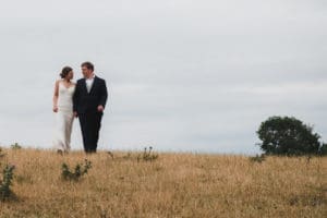 Hiring a professional Wedding photographer - a bridal couple walk through a field of parched grass