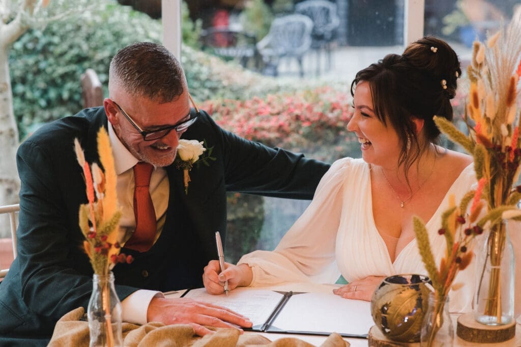 Sheene Mill Weddings in Cambridgeshire - bridal couple signing the registry, smiling and laughing