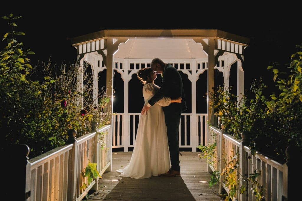 Sheene Mill Weddings in Cambridgeshire - A bridal couple hold each other in the night under a beautifully lit gazeebo