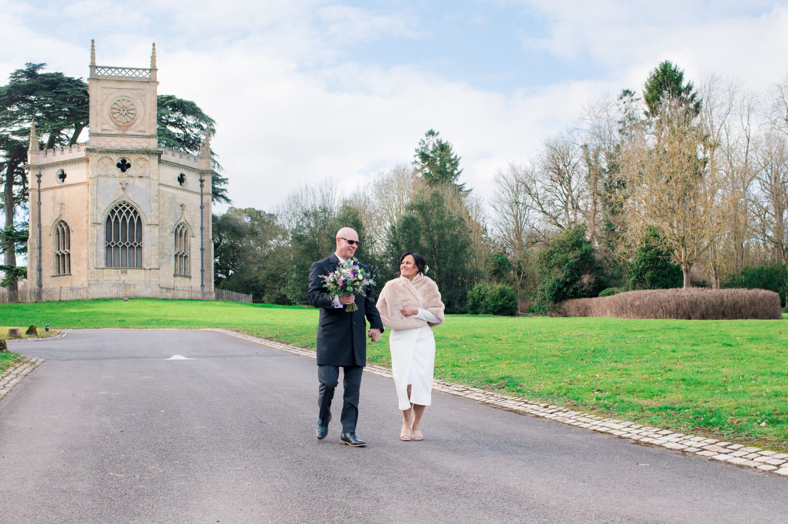 Hartwell House Wedding in Buckinghamshire - Just married couple walking down a slight hill with an old church in the background