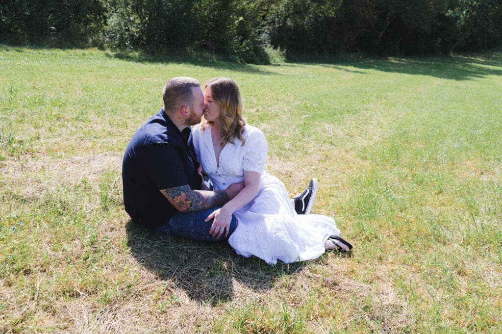 A couple are sat on the grass kissing