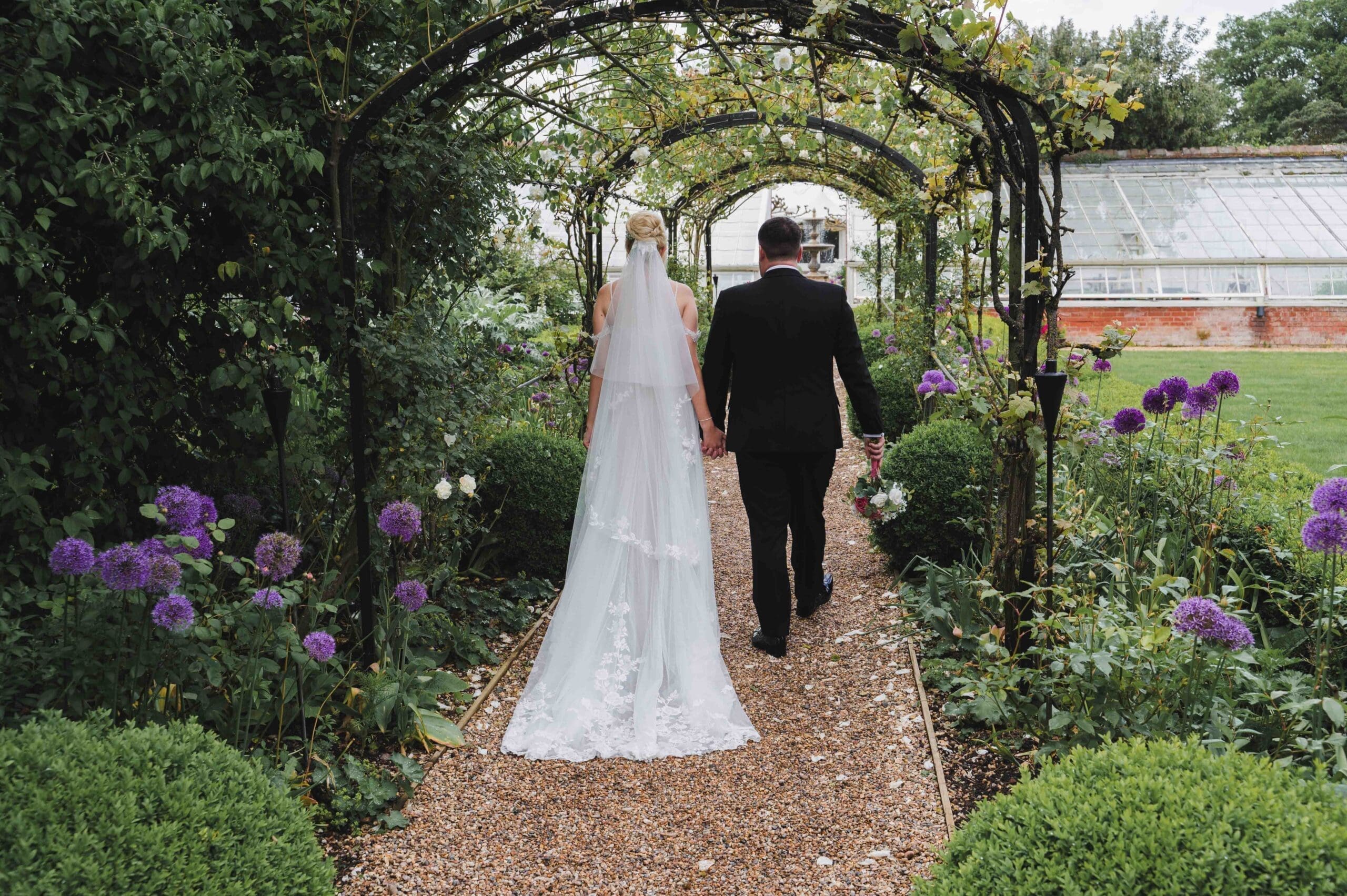 bride & Groom walking through the plant covered walkway at Braxted Park wedding venue