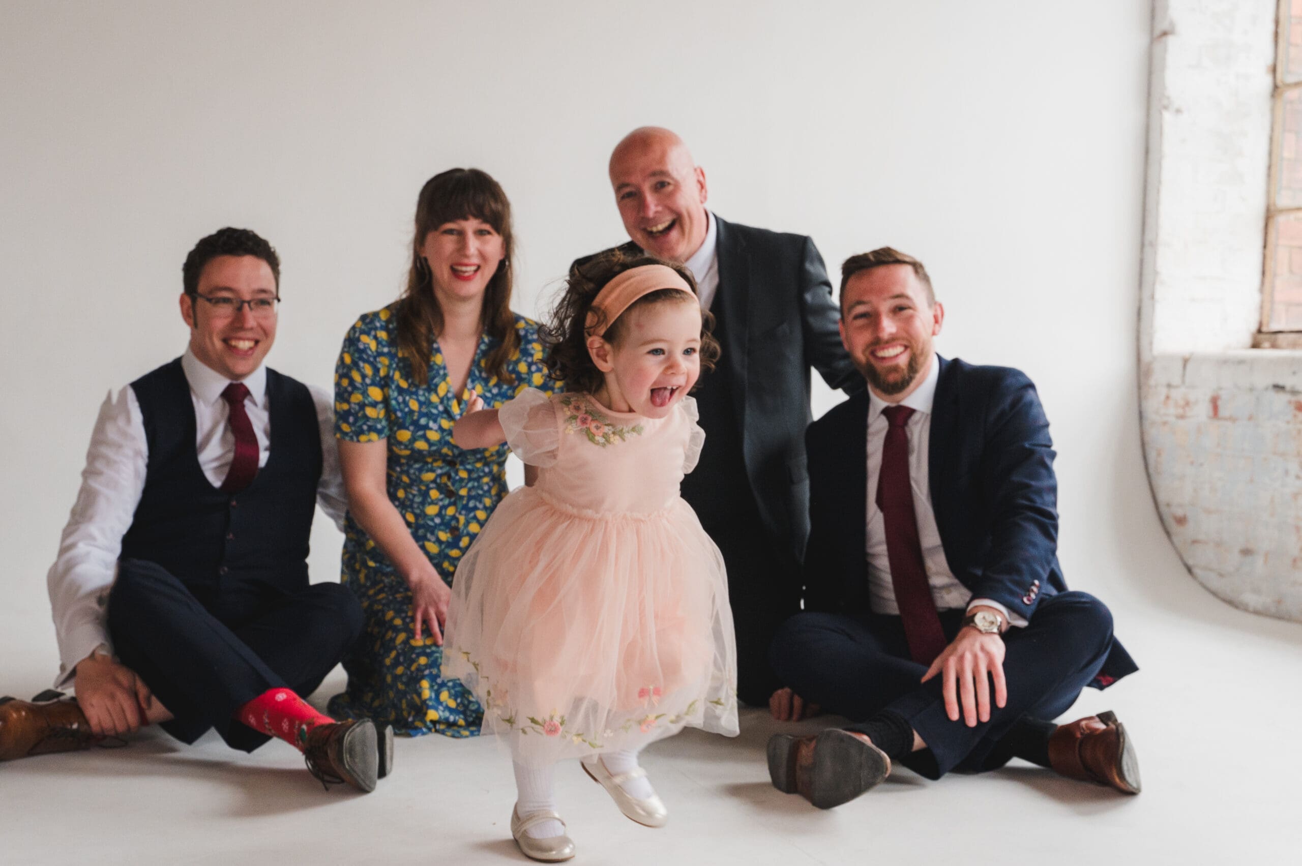 Professional Family Photography prices Bedfordshire a family sat on the floor with a little girl running forward in a pretty apricot dress