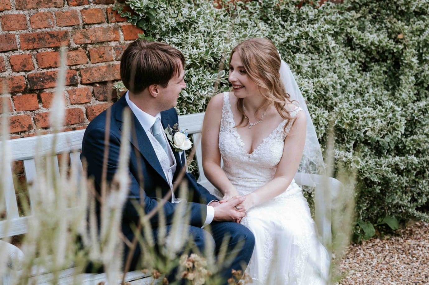 wedding photography prices - a bride and groom sit on a bench in a walled garden, gazing into each other's eyes.