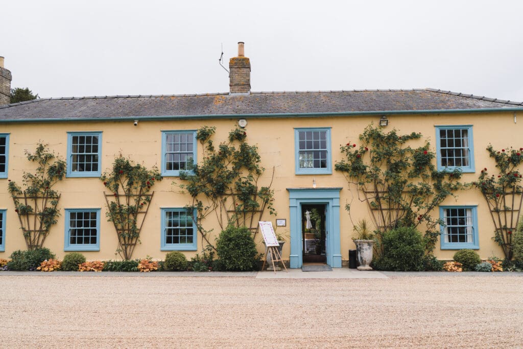 South Farm Wedding Venue - a pale cream/yellow building with sky blue window and door frames and plants climbing on the walls