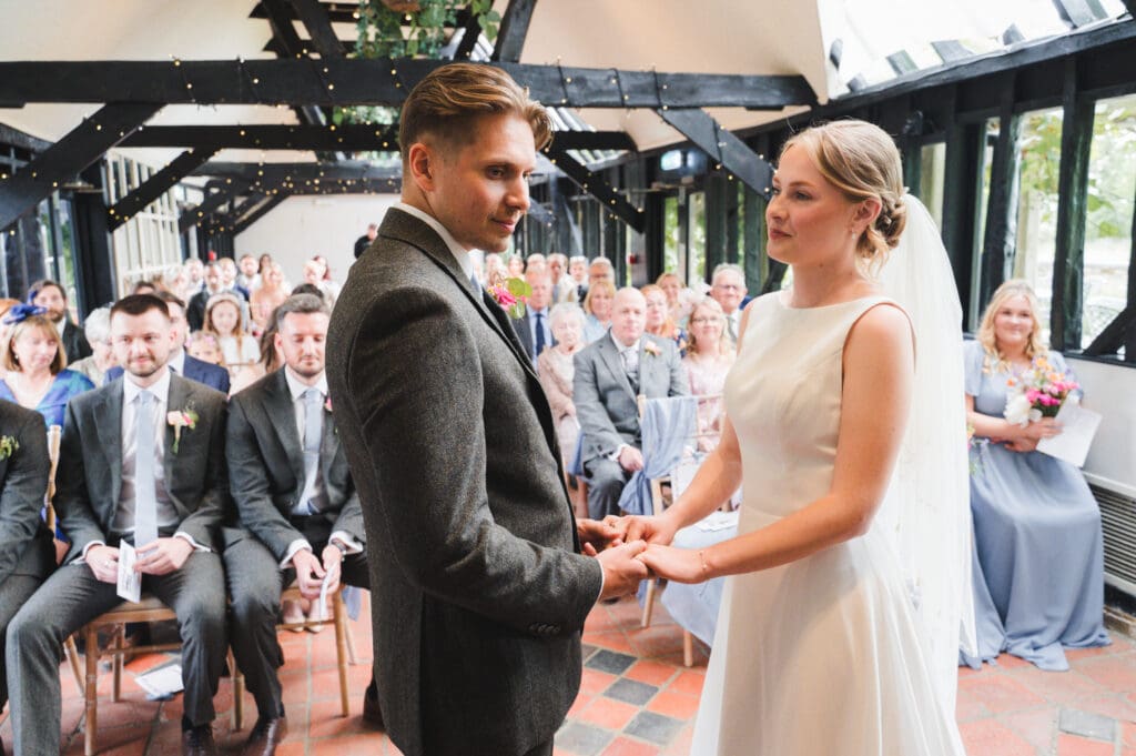 South Farm Wedding ceremony in a beamed room - the bride and groom are holding hands as guests look on 