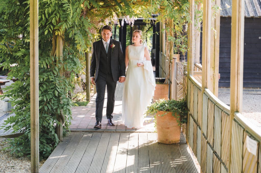 The bride and groom walk through a pergola dripping in foliage at South Farm