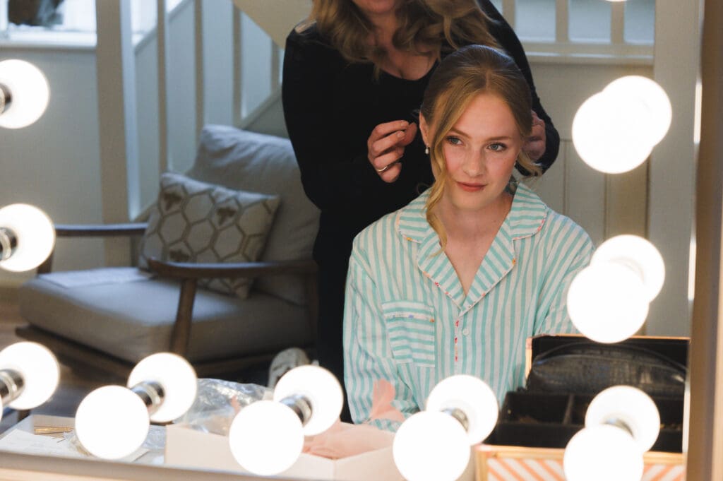 South Farm Wedding Venue Bridal Prep - bride dressed in PJs looking in the mirror as her hair is pinned up