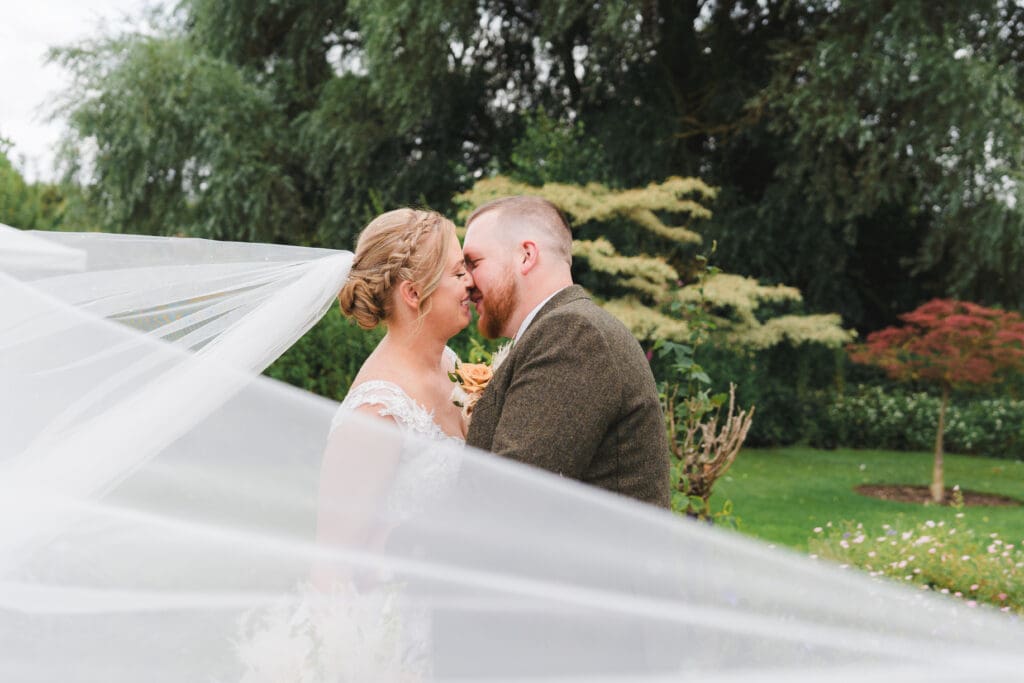 Wedding in Bedfordshire Bride and groom kissing in the grounds of their venue, the brides veil is sweeping in the wind